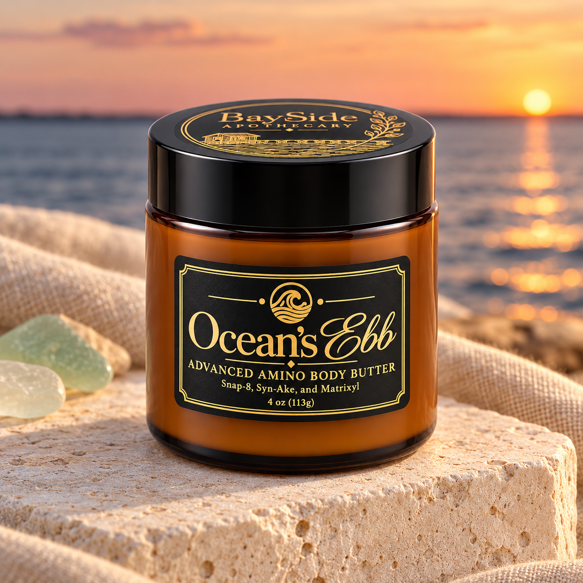 Ocean's Ebb body butter in its amber jar on pale stone beside the bay at sunset.
