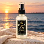 Ocean's Ebb lotion bottle beside linen on pale stone overlooking the bay at sunset.