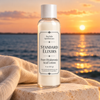 Standard Elixirs hyaluronic acid lotion bottle on pale stone beside the bay at sunset.